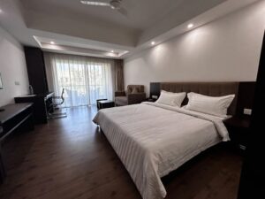 Spacious, modern hotel room with a king-sized bed, seating area, and private balcony for a comfortable Durga Puja Staycation in Kolkata at Jagriti Stays.
