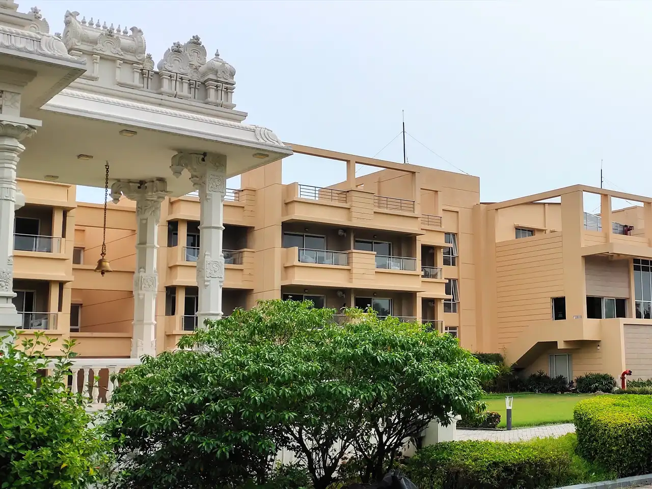 Front view of the Jagriti Dham estate among lawns and palms